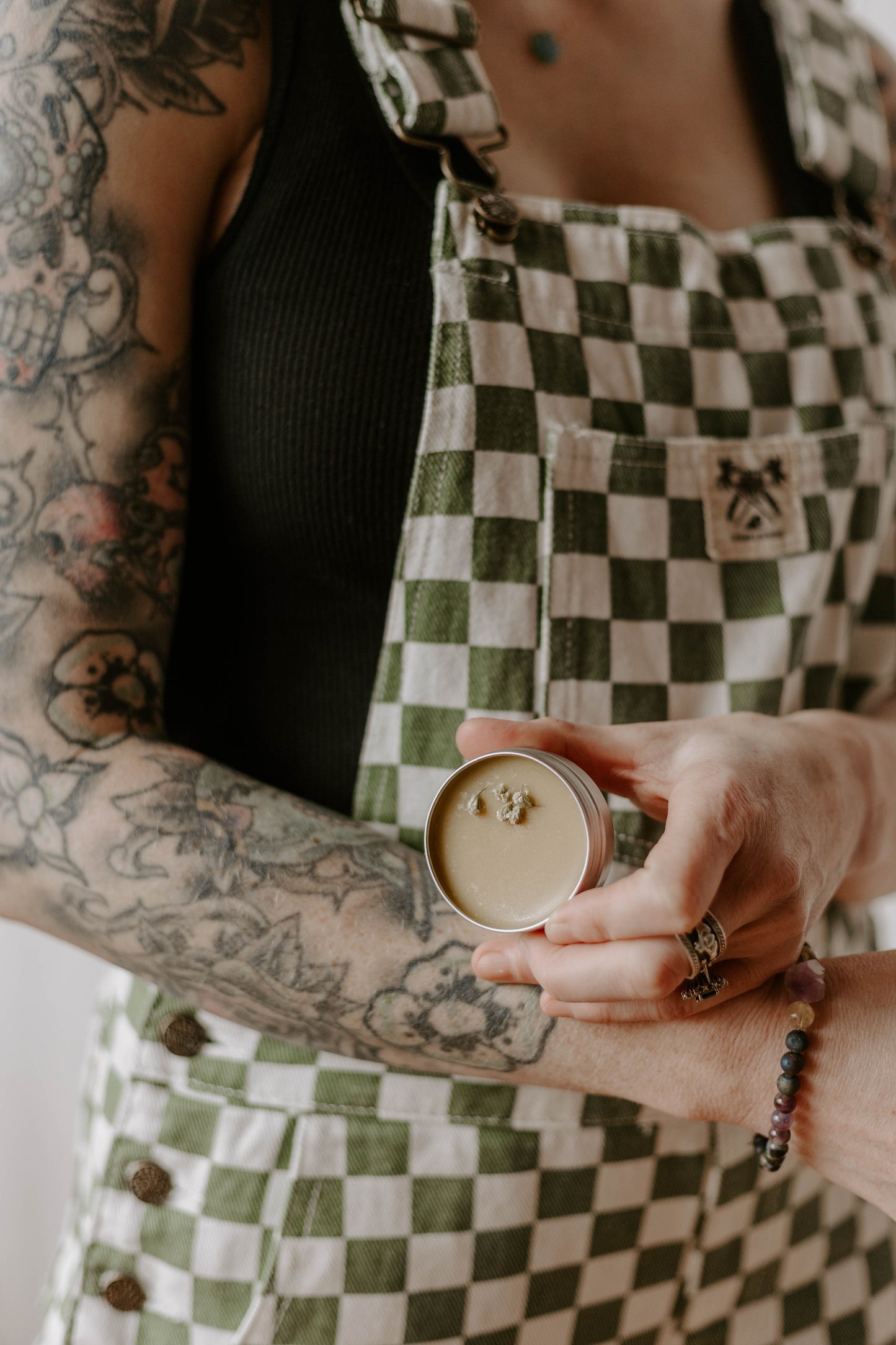 checkered overalls, green and white, black tank top, tattoos, tattoo sleeve, just a phase, balm, salve, tin, yarrow, healing, repairing, crystal bracelet.