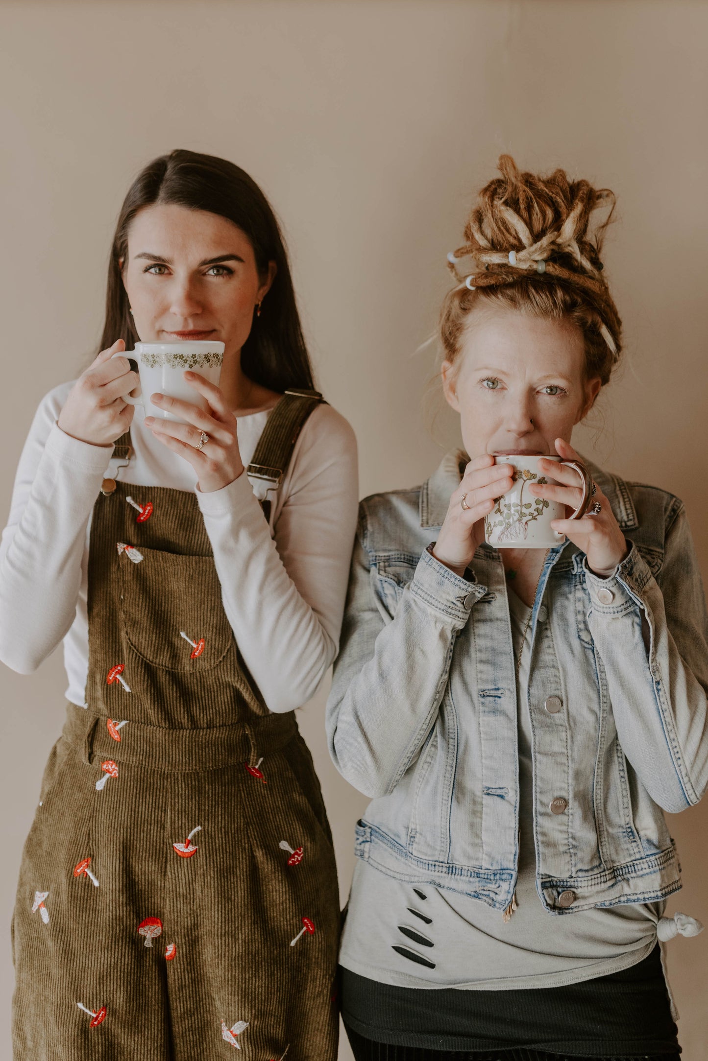 two girls drinking hot tea. hot tea. herbal tea. jean jacket. dreadlocks. mushroom overalls. brown hair. long hair.