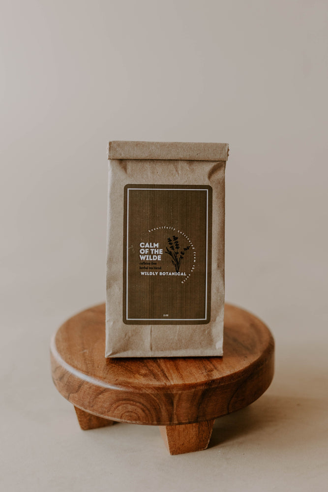 A bag of loose-leaf herbal tea blend containing chamomile, peppermint, lavender, rose, oatstraw, passionflower, lemon balm, and valerian. Kraft bag on wooden stand. brown bag with brown label.